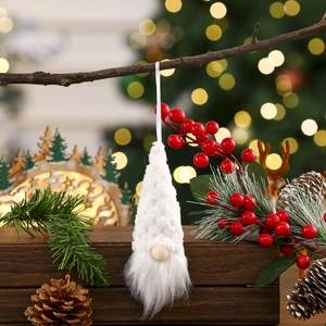 Knitted white Christmas gnome ornament hanging on a pine tree with warm festive bokeh lights
