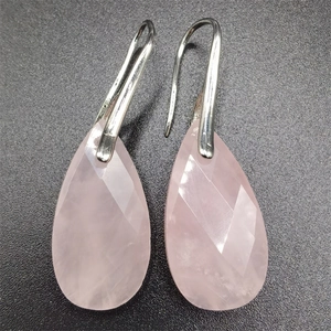 Macro shot of faceted pink quartz teardrop earrings with silver metal hooks on dark base
