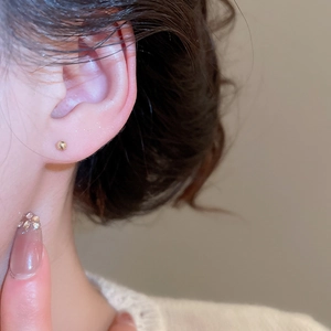 Close-up of a minimalist golden ball stud earring worn on ear with soft metallic glow