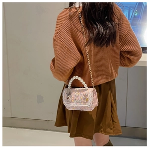 Detail of pink tweed girl's bag with pearl handle and metal chain strap on model