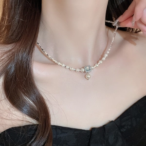 Close-up of pearl necklace with square blue gemstone pendant on model neck