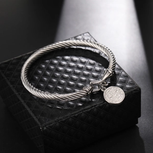 Detail of silver twist rope cable bangle with a St. Benedict medal on black jewelry box