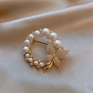 Close-up of golden butterfly brooch with pearls on soft beige silk background