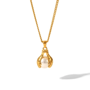 Detail of a gold hand claw pendant holding a white pearl on a delicate fine chain