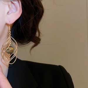 Close-up of model wearing twisted geometric gold drop earrings with tiger eye stone beads