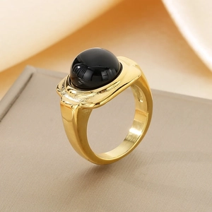Dettaglio macro di un anello a fascia larga in oro con grande gemma nera tonda lucida