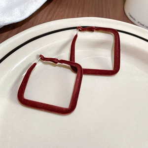 Gros plan de boucles d'oreilles carrées floquées bordeaux sur une assiette en céramique