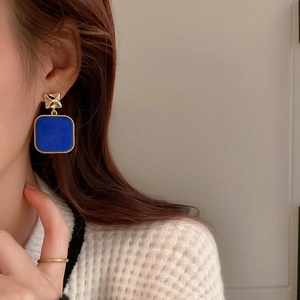 Close-up of royal blue square dangle earrings with gold geometric studs on model