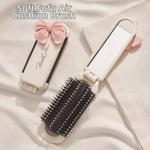 Close-up of portable folding hairbrush with built-in mirror and pink bow in cream white