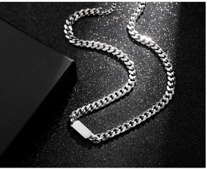 Detail of silver Cuban link necklace with rectangular tag on black textured background