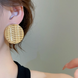 Close-up of oversized gold wavy textured disk earring on model with modern ripple effect
