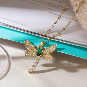 Gold-plated dragonfly pendant necklace with green gemstone and zirconia on paper