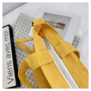 Detailed close-up of yellow canvas tote bag top zipper and sturdy handle stitching