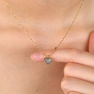 Detail of a gold heart necklace with black mother of pearl worn on a model's neck