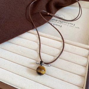 Detailed view of tiger eye stone pendant on brown braided cord in jewelry box