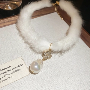 Detail of plush fur choker with clover charm and baroque pearl pendant on textured backdrop