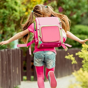 Pink ergonomic student backpack with cactus pendant shown on a girl running outdoors