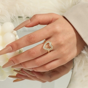 Detail of gold hollow heart ring with white crystals on female finger with beige suit