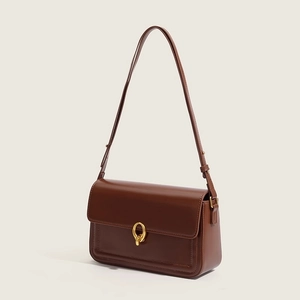 Detail of premium brown leather shoulder bag featuring round gold metallic buckle hardware
