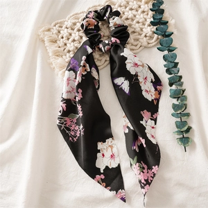 Detail of a black floral satin hair scrunchie with long ribbons on textured fabric