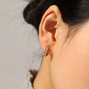 Gros plan détaillé de boucles d'oreilles huggie dorées avec cinq zircons taille baguette