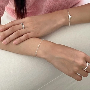 French style silver heart rings and delicate pearl bracelet set on wrist