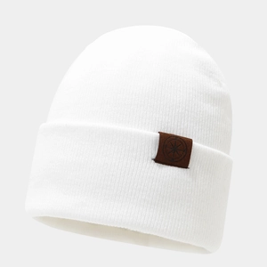 Gros plan du bonnet en maille blanche avec un écusson en cuir à motif boussole