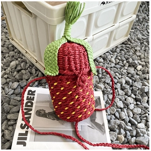 Close-up of strawberry-shaped woven straw shoulder bag with green leaf detail on a magazine