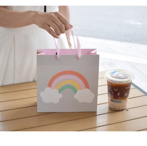 Close-up of gray gift bag with rainbow pattern, pink ribbon handle on wooden table