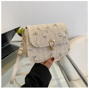 Detail of beige straw crossbody bag featuring green floral embroidery and gold metal clasp