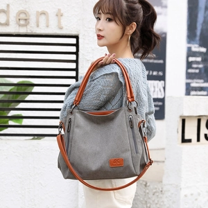 Minimalist grey canvas shoulder bag with brown leather handles and brand logo patch