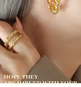 Macro detail of gold-plated twisted C-shape earrings and lava texture rings on model