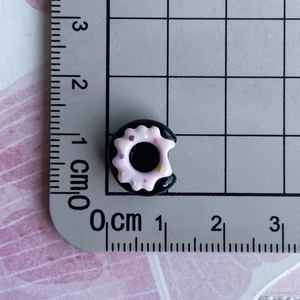 Macro view of a 1cm mini resin donut charm with black base and pink frosting on a ruler