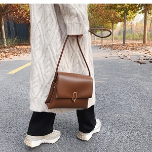 Sac bandoulière carré en cuir marron avec boucle dorée porté par un mannequin en automne