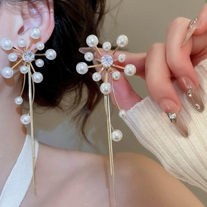 Detailed shot of flower pearl earrings with long golden tassels on a female model