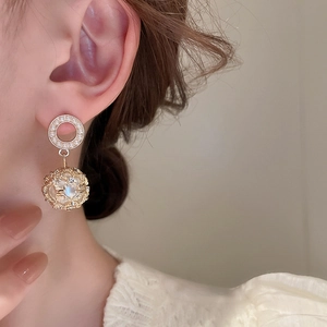 Close-up of model wearing gold lattice hollow cage earrings with faux pearl accents