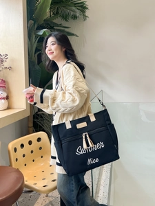 Detail of black canvas tote bag with white embroidery and beige straps for daily use