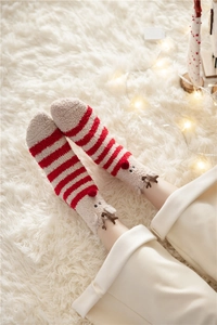 Close-up of fuzzy Christmas reindeer socks in red and cream stripes on plush rug