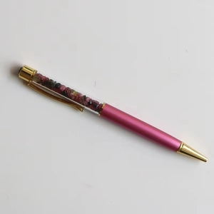 Detail of pink metal ballpoint pen with transparent barrel filled with colorful crystals