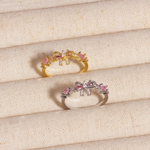 Detail of bow-shaped rings with pink heart zircons in gold and silver finishes