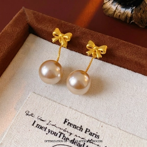 French vintage gold bow earrings with hanging pink pearl on rustic linen background