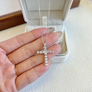 Close-up of a silver cross pendant with cubic zirconia stones held in hand