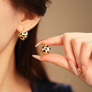 Macro detail of gold-tone heart earrings with black cow pattern on a female model