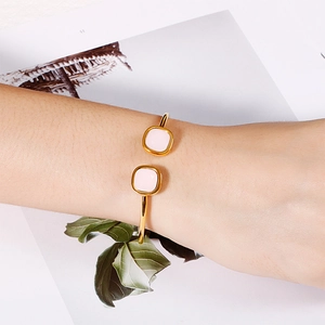 Close-up of golden hollow square open bangle with pink details on a fashion magazine