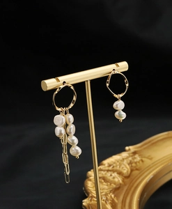 Detail of asymmetric baroque pearl earrings with golden tassels on display stand