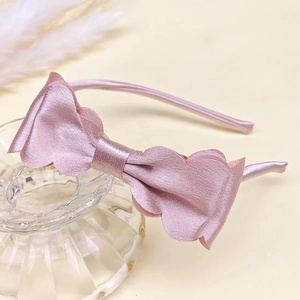 Close-up of a pink satin bow headband with ruffled edges on a glass display