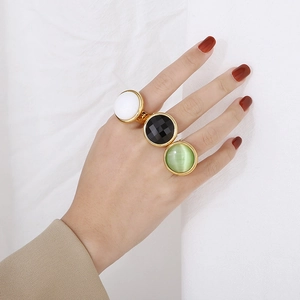 Three luxury gold rings with white, black, and green stones worn on a model's hand