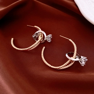 Detail of gold twisted C-shape earrings with clear gemstone and silver ring charms