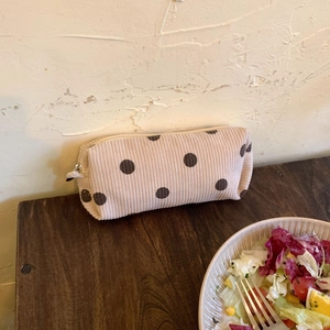 Close-up of beige corduroy pouch with brown polka dots and zipper on a wooden table