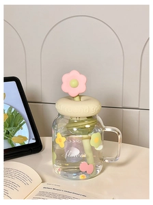 Detail of cute glass cup with flower straw and pastel handle on a desktop